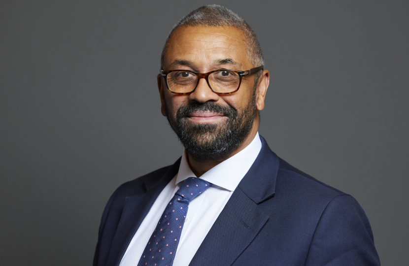 James Cleverly wearing a dark suit jacket with a white shirt and a blue tie with pink dots